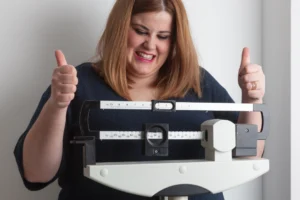 A happy woman giving a thumbs-up while measuring her weight on a scale, showing the effectiveness of Semaglutide.